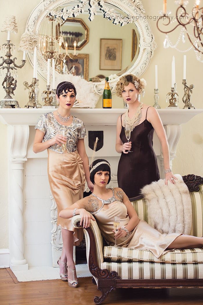 champagne flutes in the hands of three women, each dressed in a gatsby themed dress, pale peach silk with silver embroidery, black satin slip-style gown, in a room with classical decor