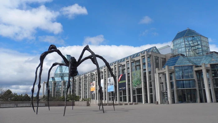 sculpture of a giant black spider, near a building, made of concrete and glass, supported by off-white columns, postmodernism examples, canadian national gallery