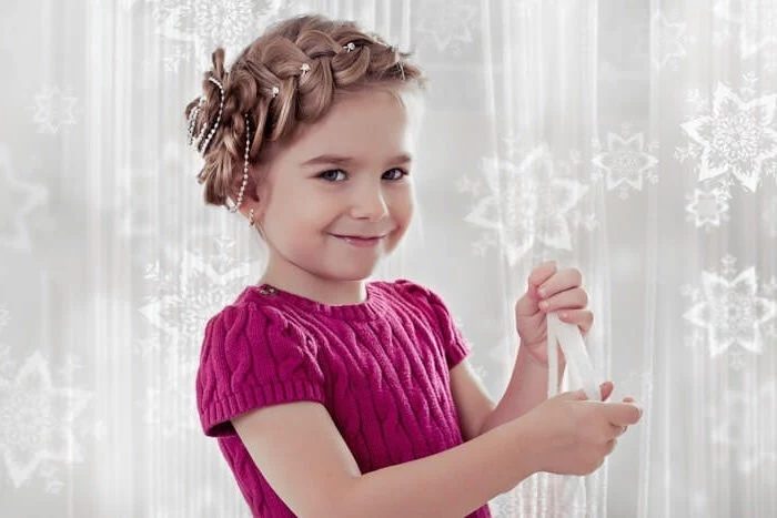 knitted pink sweater, with short sleeves, worn by a smiling young child, with light brunette hair, styled into a crown braid, around her head