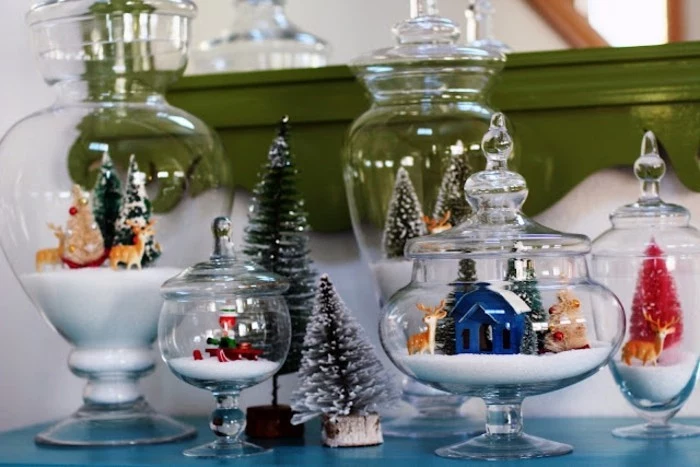 several clear glass containers, in different shapes and sizes, with ornate lids, each containing faux snow, and christmas-themed figurines, homemade gift ideas, tiny fir trees