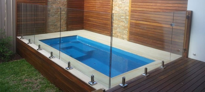 panels made from clear glass, surrounding a blue rectangular pool, built in the corner of a yard, backyards with pools, patio and lawn