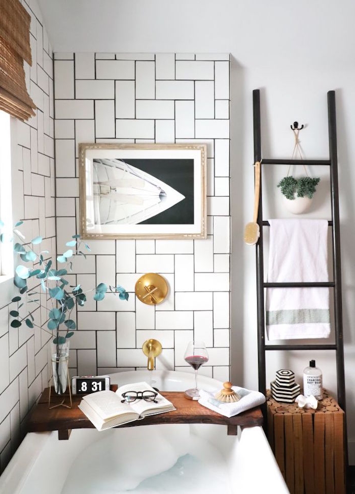 open book and a glass of red wine, reading glasses and a vase, with a green plant, placed on a wooden tray, over a white bathtub, diy bathroom décor, white herringbone subway tiles