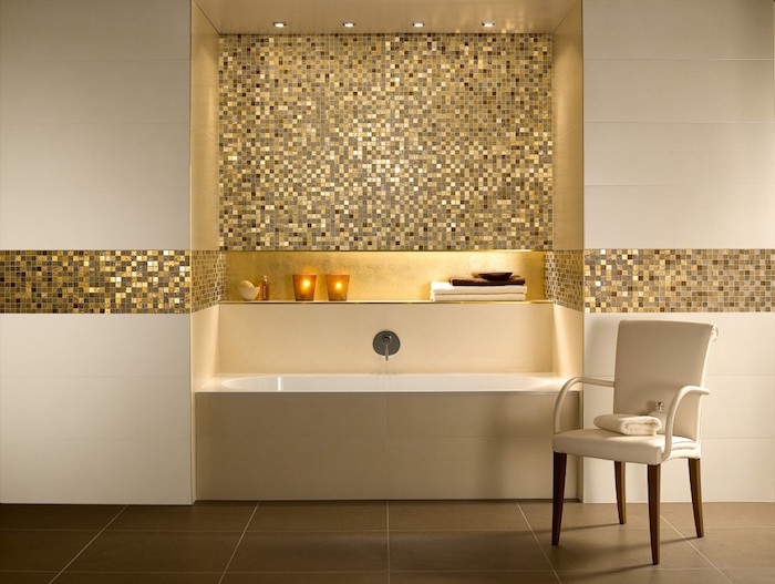 minimalistic bathroom in cream and gold, with a rectangular tub, and a chair, glittering gold mosaic, brown tiled floor