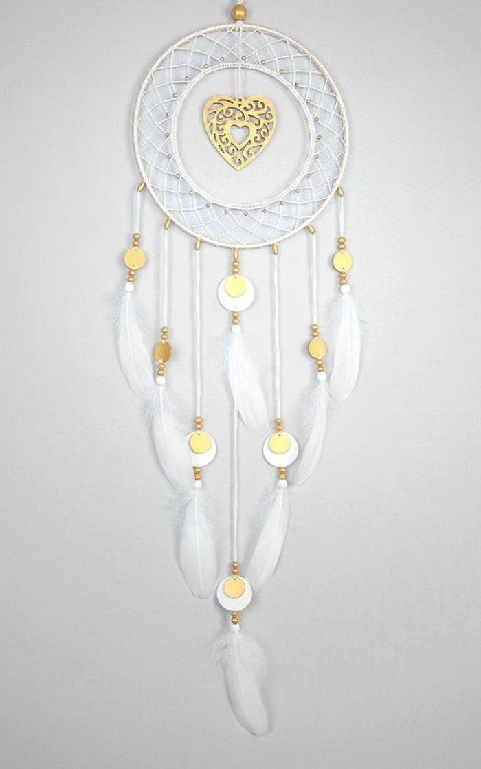 heart ornament in gold, in the middle of a white dream catcher, with white feathers, and more small gold ornaments