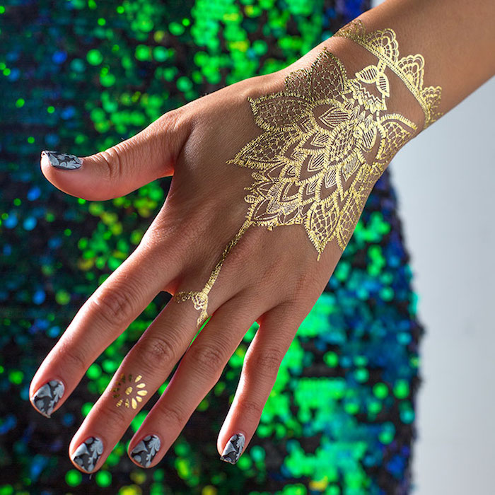imitation of a henna tattoo, made with golden paint, henna meaning, on a slim hand, with black and grey nail polish