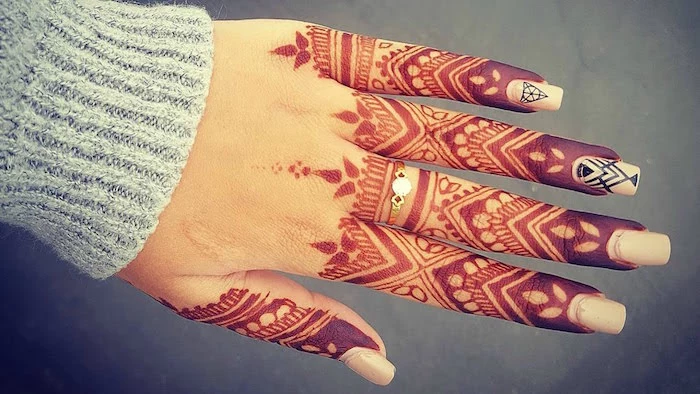 pale grey knitted sleeve, on a hand with finger henna, in dark brown and orange, with a golden ring