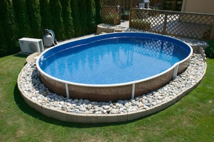 oval pool filled with water, resting on a bed of white stones, in a yard with green grass, small above ground pools, wooden fence nearby