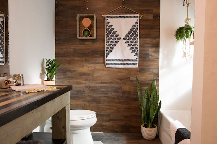 wooden panelling in brown, on one of the walls of a room, with a massive wooden table, a toilet and a bathtub, nice bathrooms, potted plants and a wall decorations 