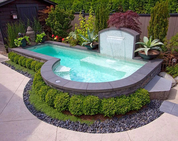 fountain pouring water into a small pool, lined with grey tiles, and decorated with small green shrubs, and various other plants