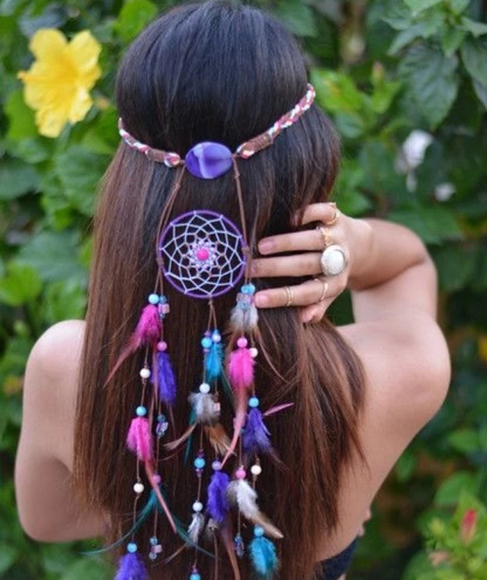 brunette woman with long hair, wearing a small, purple dream catcher, decorated with tiny pink, white and turquoise feathers, in her hair, pictures of dream catchers, leafy green plants, with yellow blossoms in the background