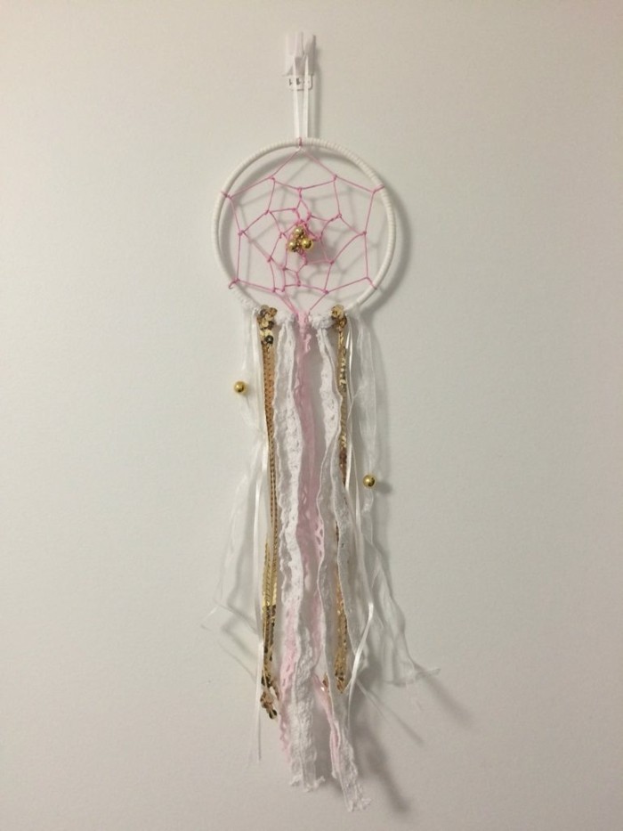 off-white wall, decorated with a white dreamcatcher, how to make a dreamcatcher, featuring a pink net, white and pale pink crochet lace tassels, gold chain details, and gold beads