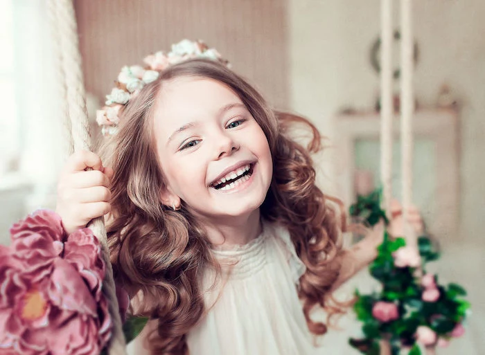 hairstyles for little girls, laughing child with long, curled brunette hair, wearing a flower crown