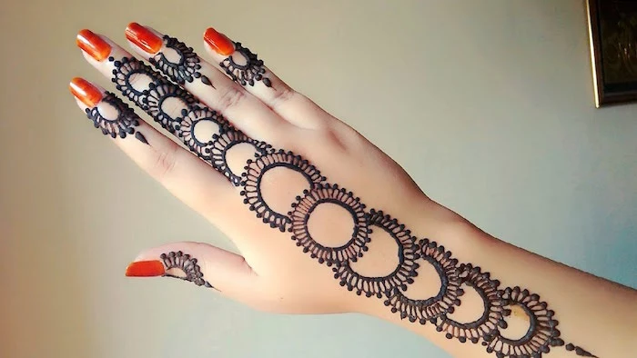 bright orange nail polish, on a hand, decorated with henna hand tattoo designs, featuring decorative circles, running from the wrist, to the tip of the middle finger