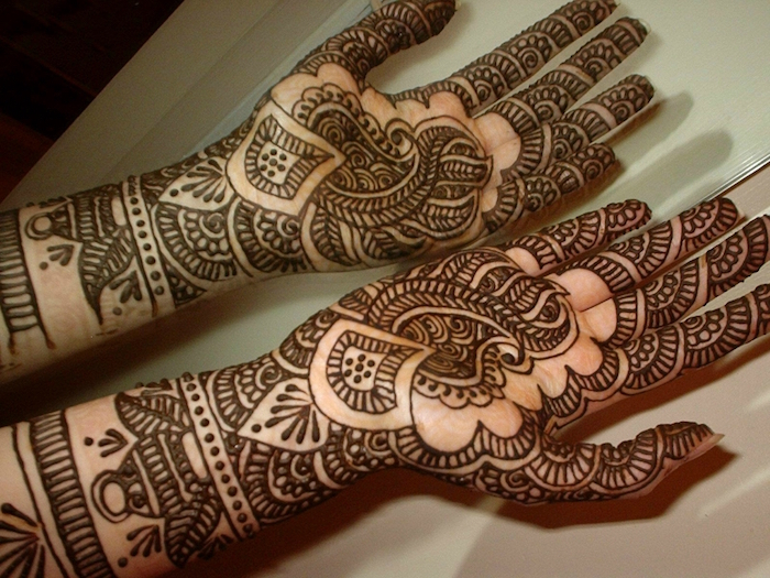 set of hands, with outstretched palms, fully covered with henna hand tattoo designs, in a dark brown hue