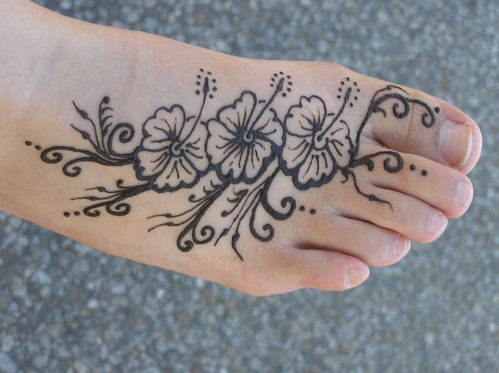 cute henna, three hibiscus flowers, decorated with dots and flourishes, drawn on a person's foot