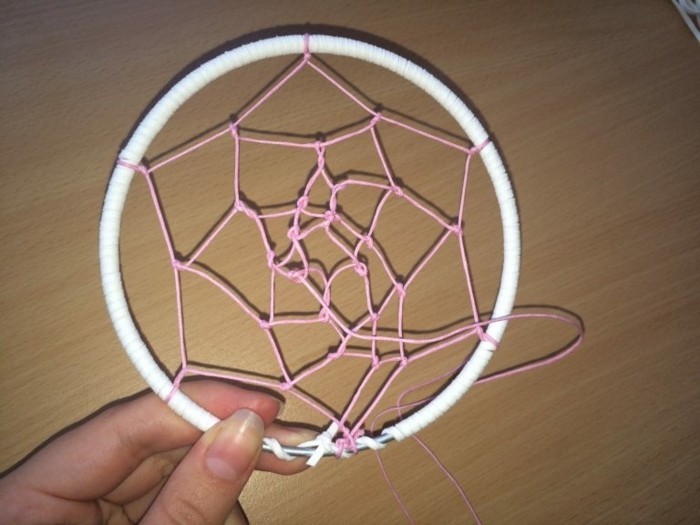 finished woven pattern, made of pink thread, and tied to a white hoop, how to weave a dreamcatcher, held by a hand