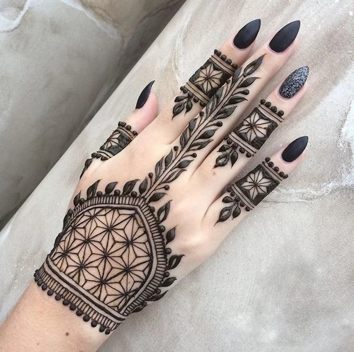 stars and leaves, and other shapes, painted in black henna, on a pale hand, with long and sharp black nails