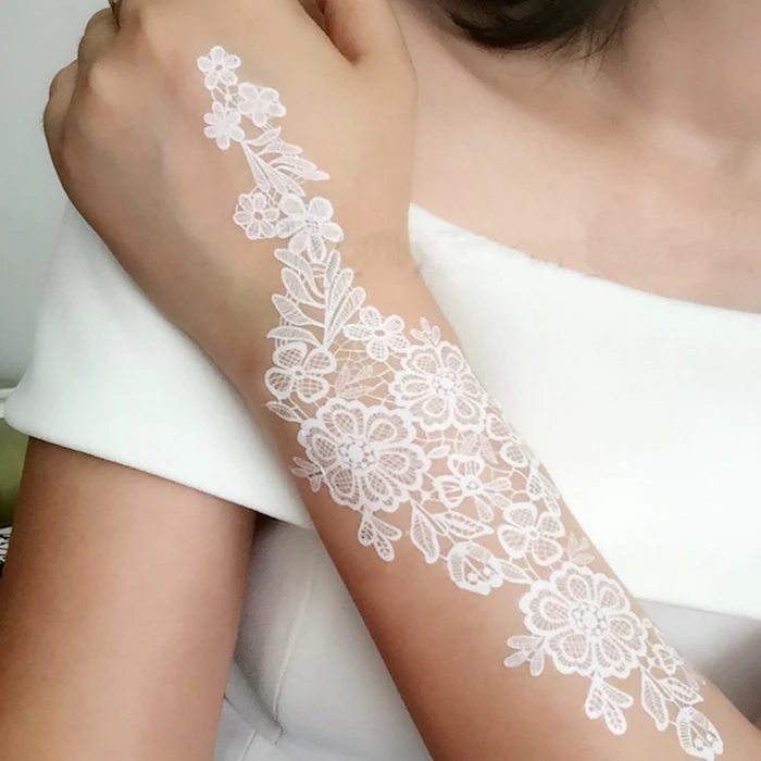 temporary henna tattoos, lace-like white henna tattoo, with floral motifs, on the forearm of a woman, dressed in a white top