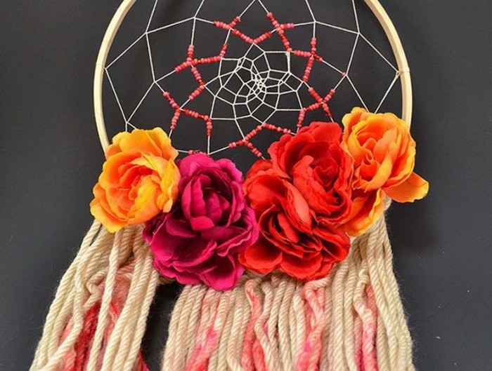 five faux roses, in yellow and orange, and deep red, decorating a dream catcher, with beige and pink tassels, dreamcatcher designs, seen in close up