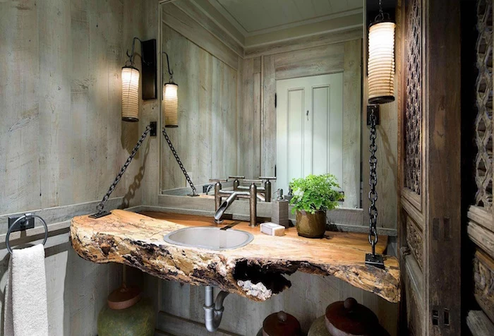 counter made from a large piece of untreated wood, with and inbuilt sink, suspended from a wall, using black chains, a large wall mirror, and wood panelling on the walls, modern bathroom ideas, two lantern lamps, and an ornamental wooden door