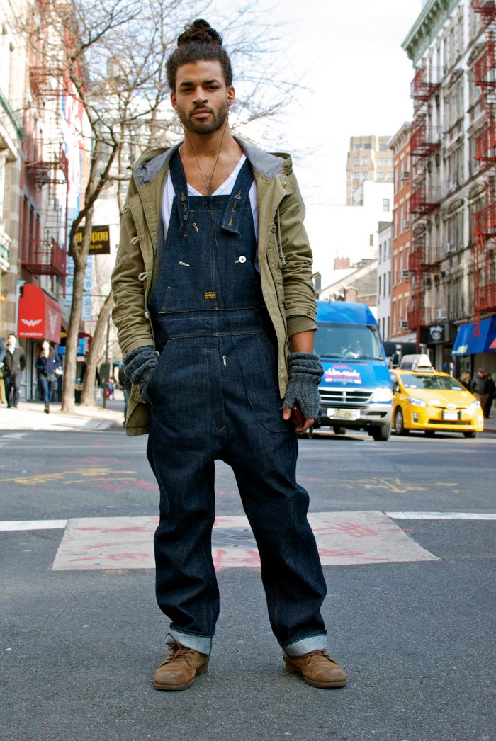 man bun worn by a young man, with beard and mustache, wearing baggy retro denim overalls, worker's boots and a khaki green parka, 90s inspired outfits, over a white t-shirt