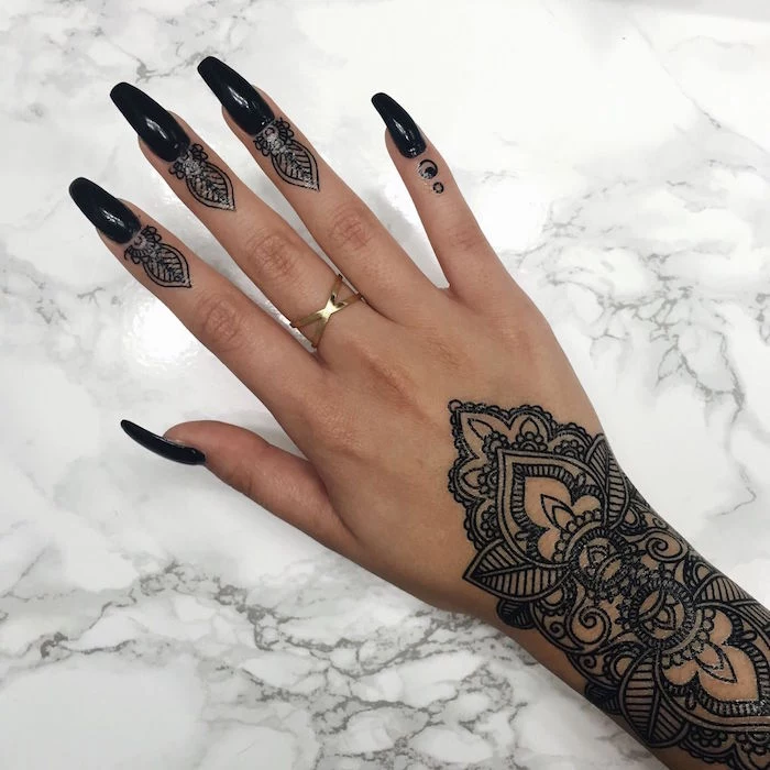 real tattoo in black, inspired by mehndi, decorating the wrist and fingertips, of a hand with long, ballerina-shape nails, painted in black