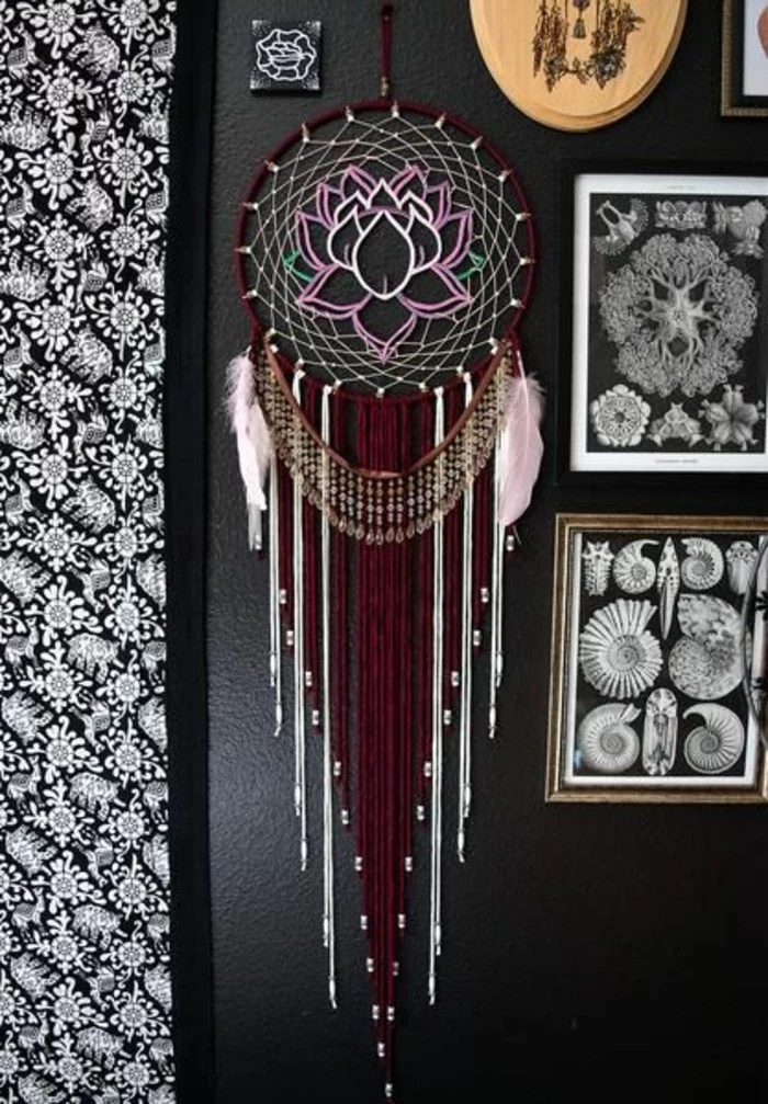 framed images and others, hung on a black wall, near a large dream catcher, with brown and white tassels, two pale pink feathers, and a lotus detail