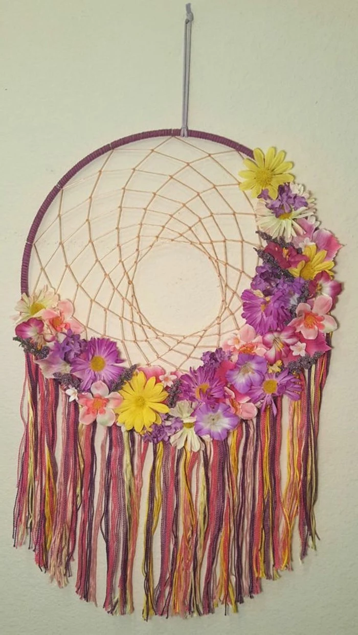 yellow and purple, cream and pink flowers, of different kinds, decorating a dream catcher, with many multicolored tassels, big dream catchers
