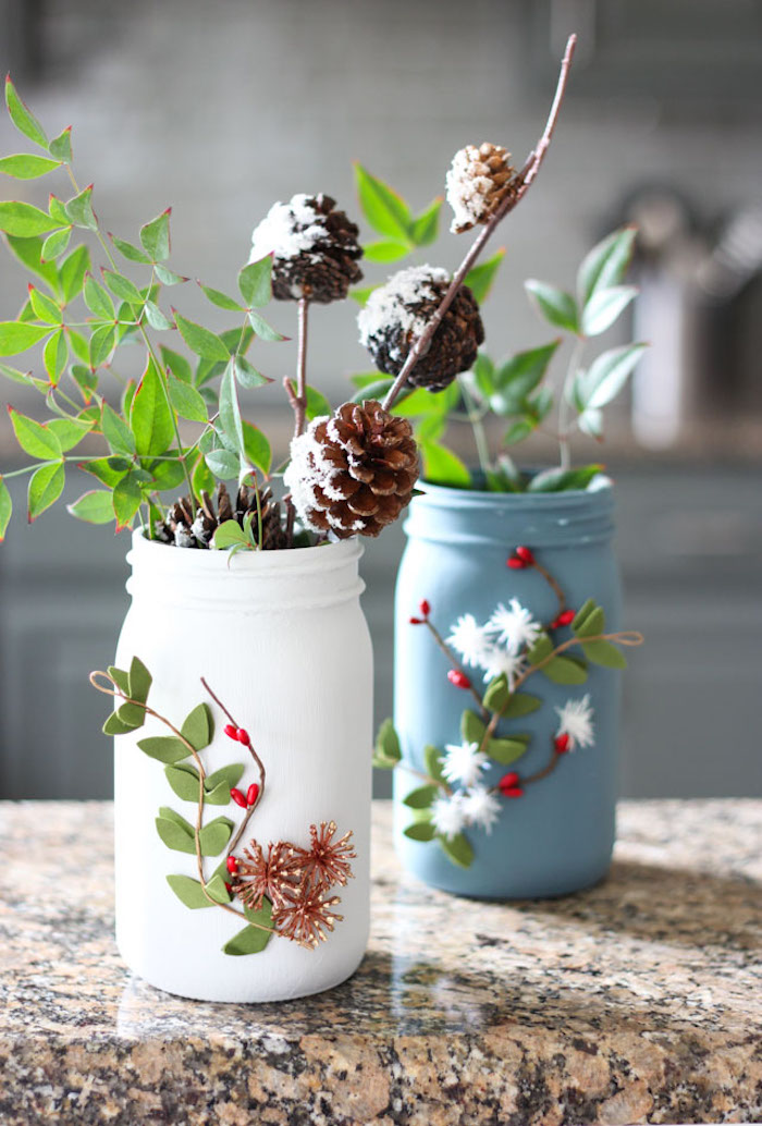 two mason jars painted in blue and white, flowers and pine cones inside, felt faux flowers glued to the front, creative gift ideas