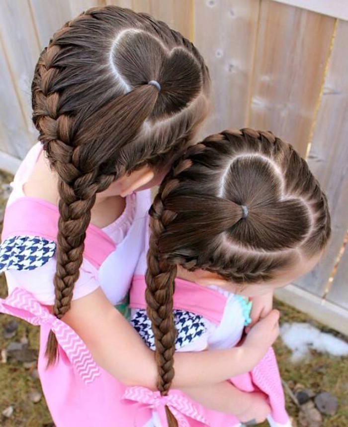 sisters with matching hairstyles, two children with identically braided, long brunette hair, forming a heart-shape, on top of their heads, wearing the same clothes and hugging