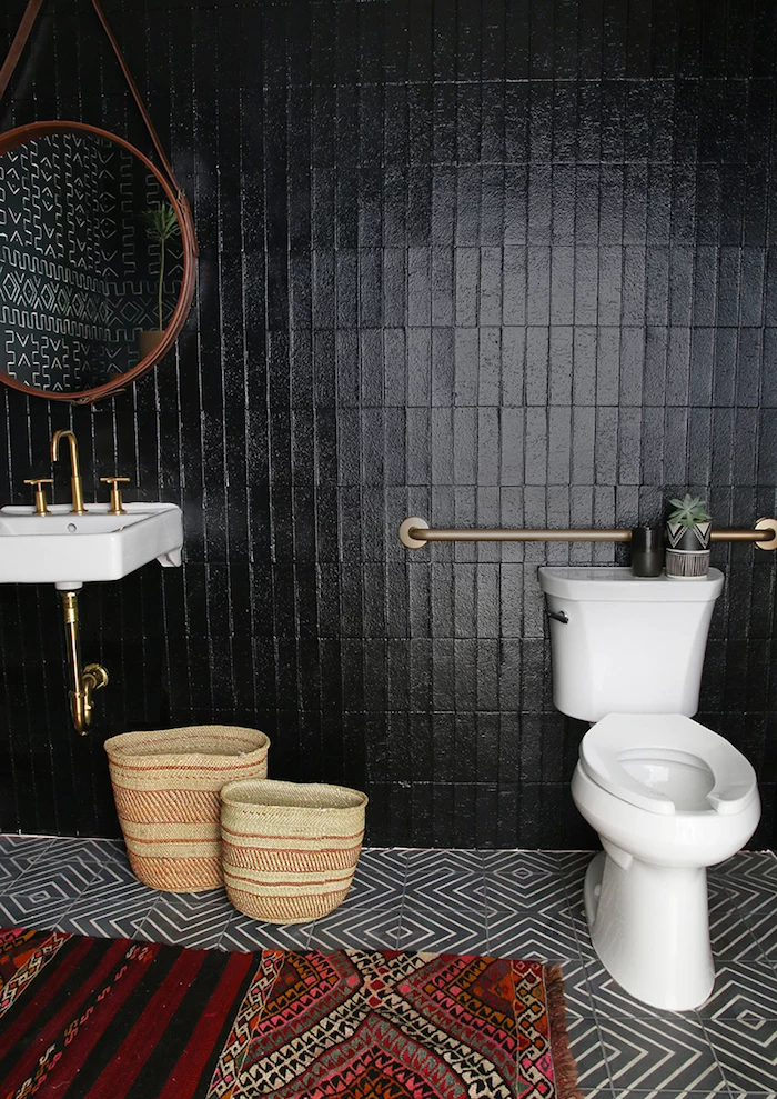 jet black wall tiles, in a room with a black and white tiled floor, containing a white ceramic toilet bowl, and a matching sink, bathroom wall decor ideas, multi-coloured rug with a tribal pattern