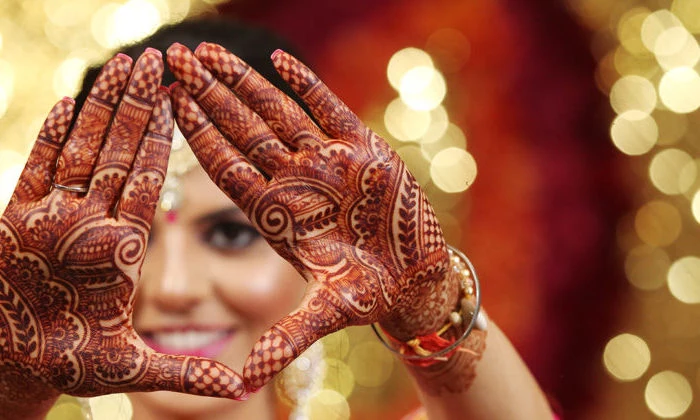 smiling indian bride, with make up and jewelry, holding her hands in front of her face, to show her palms, decorated with intricate, red henna patterns 