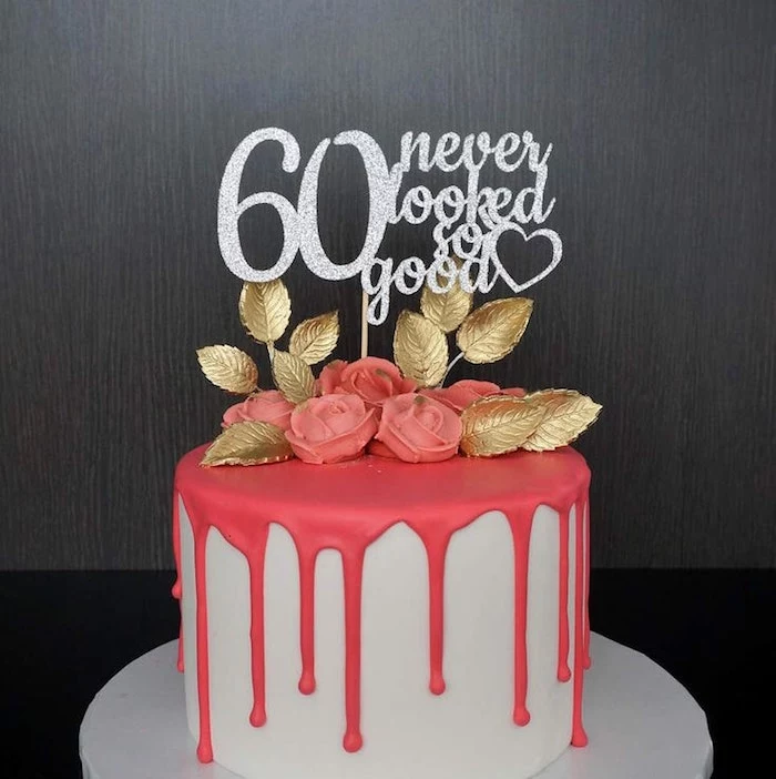 leaves made from gold fondant, and pink fondant roses, on a white cake, with a melting-effect pink frosting, and a sparkly silver topper, reading 60 never looked so good