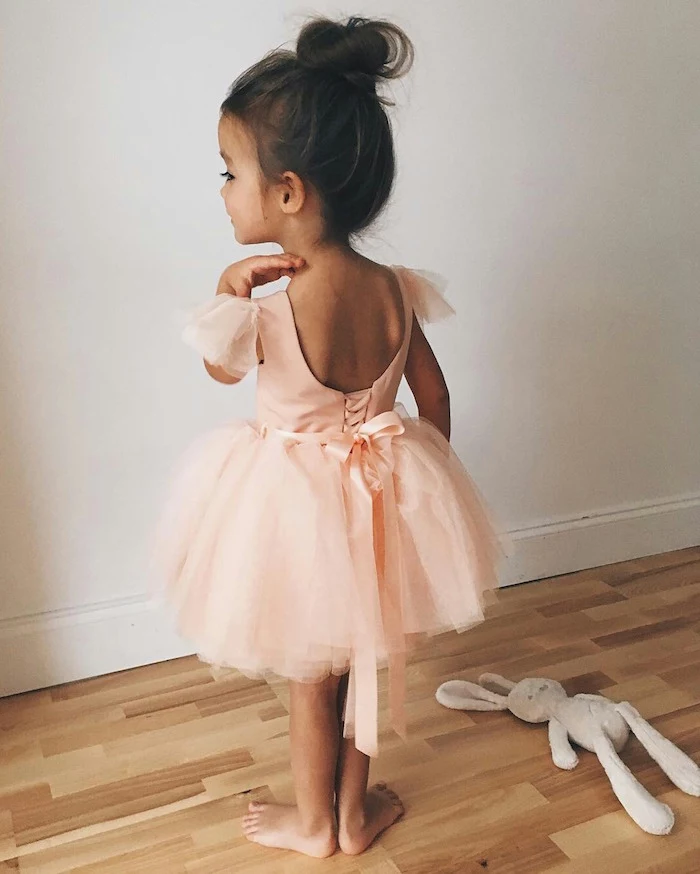 little girl hairstyles, child in a pale peach ballerina outfit, with a tulle skirt, dark brunette hair, tied in a messy top knot