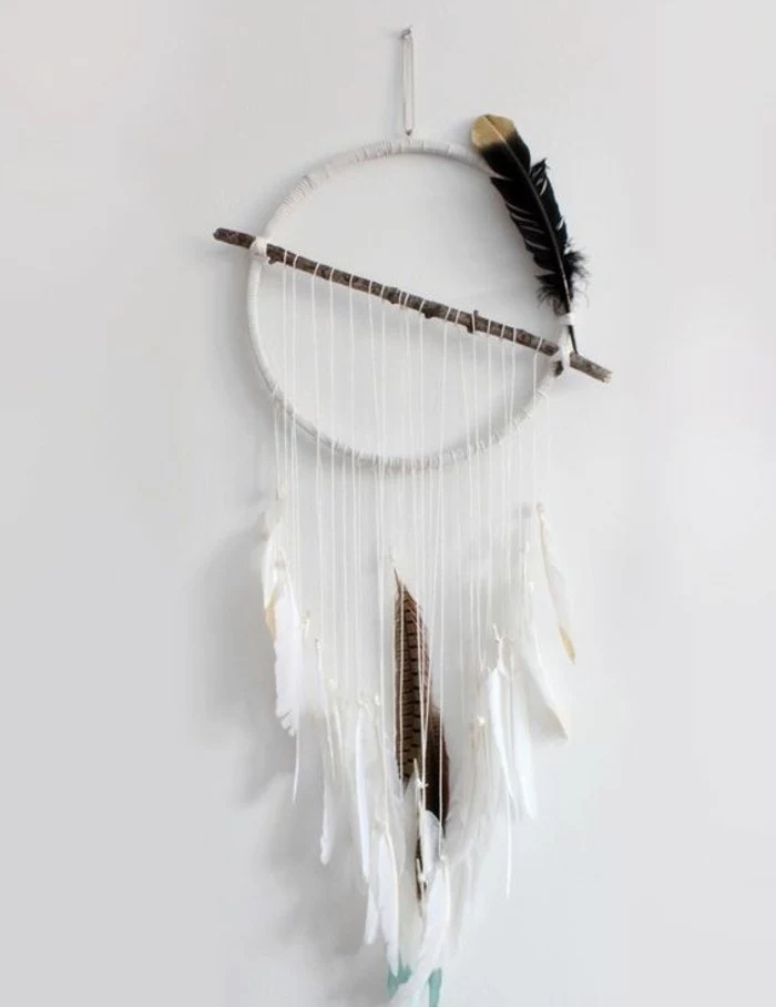 simple white diy dreamcatcher, with one brown branch, and several dark feathers, hanging on a white wall