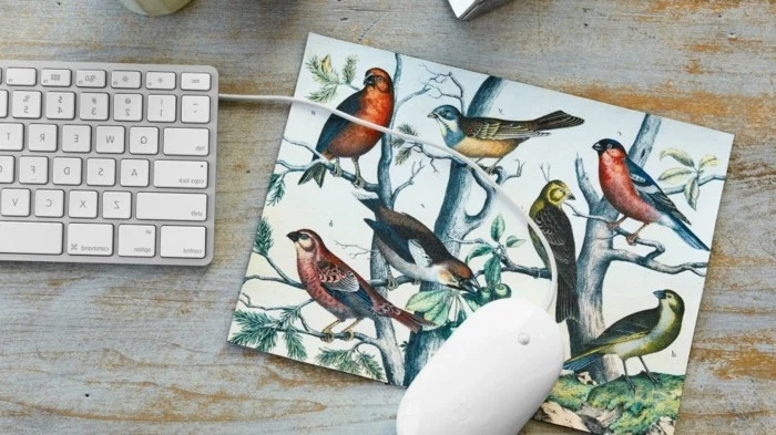 drawings of birds and trees, decorating a mousepad, with a white mouse, near a keyboard