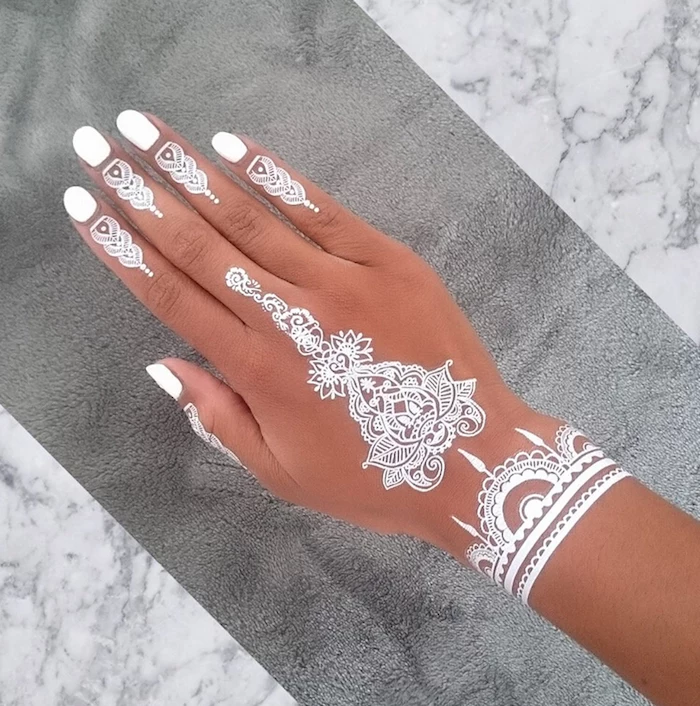 contarsting white nail polish, and a cute henna tattoo in white, on a tan hand, placed over a grey towel