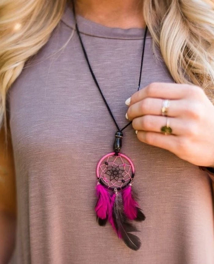 pendant shaped like a small, pink and black dreamcatcher, with feathers and tiny beads, pictures of dream catchers, worn by blonde woman, with a pale grey top