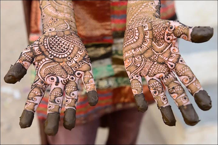 recently applied henna, on the palms of a woman, dressed in a multicolored outfit, henna hand tattoo designs, with intricate patterns