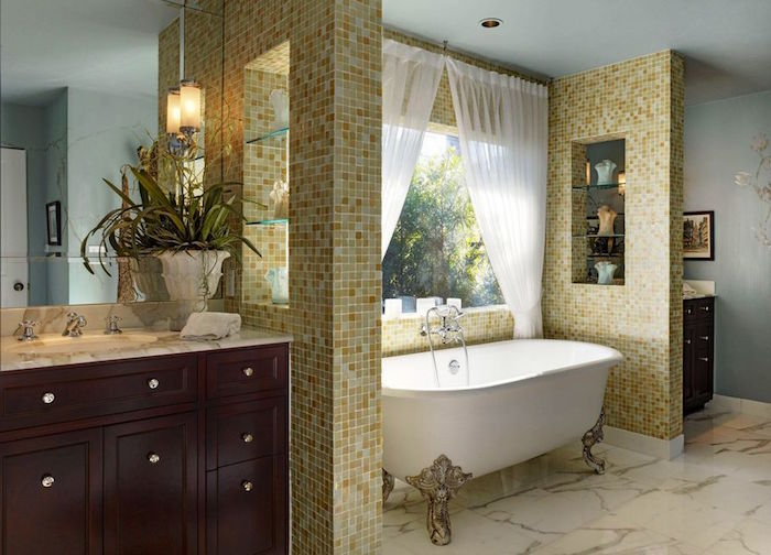 curtains in white, on a window inside a bathroom, with a marble floor, pale blue walls, partially covered in yellow mosaic, claw-footed bath, and cupboard with sink