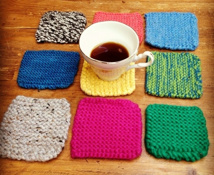 nine square knitted coasters, in navy blue and teal, pink and yellow, green and red, and mixed colors, last minute birthday gifts, half-filled teacup on one of them