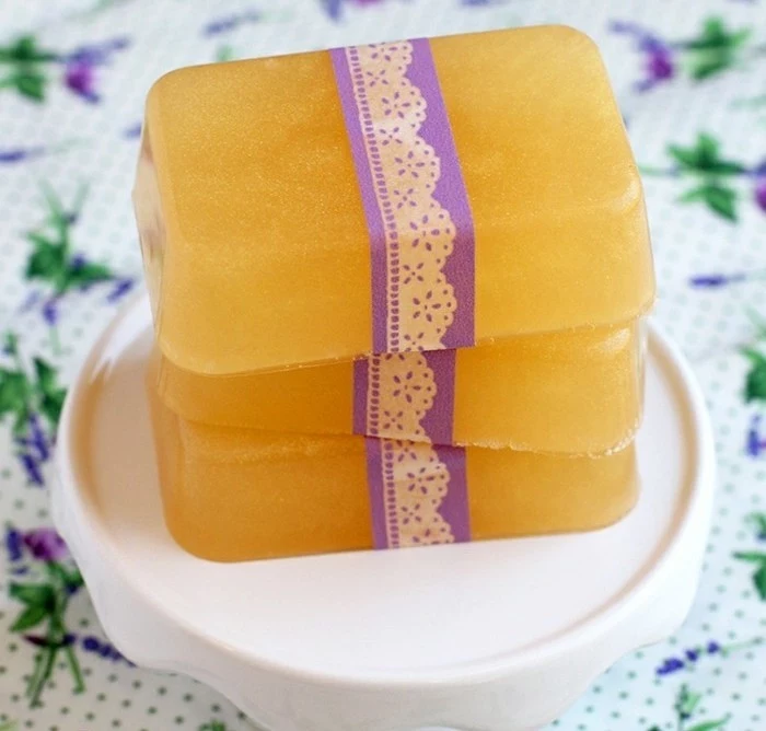 bars of orange soap, decorated with white and purple, lace like paper ribbon, handmade gifts, placed on a white dish