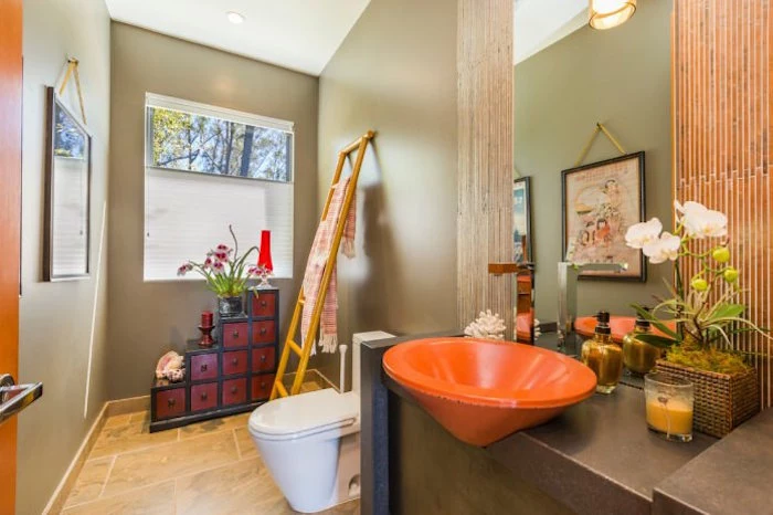 cherry red and black, east asian-style cupboard, inside a bathroom with beige walls and floor, containing a white toilet seat, and bright orange sink