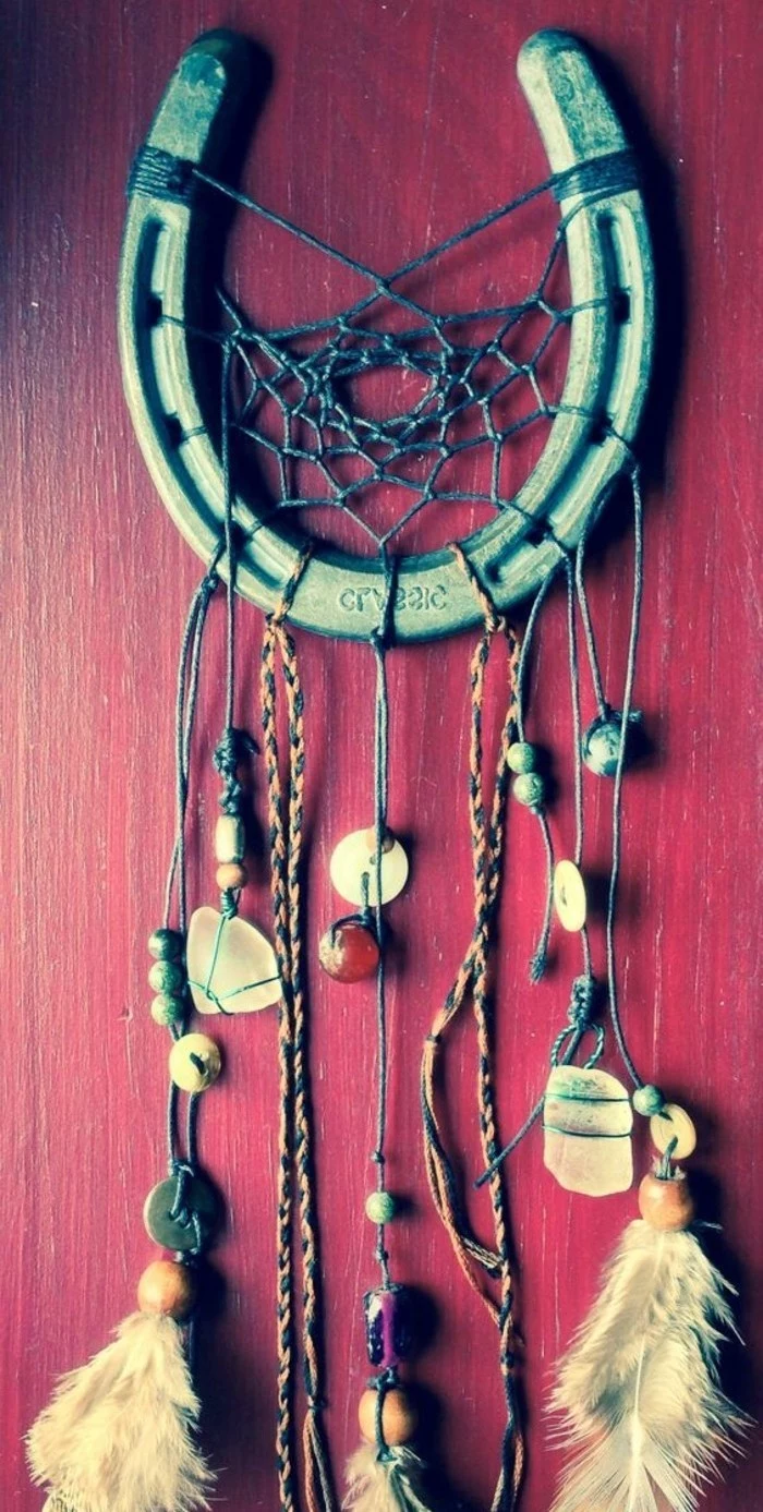 horseshoe in green, transformed into a diy dreamcatcher, with a dark teal net, and small beads, feathers and stones, tied on multicolored strings