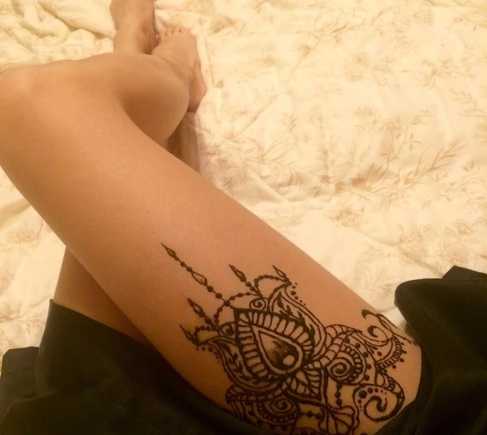 upper thigh cute henna tattoo, on the leg of a woman, dressed in a black skirt, lying on a cream duvet