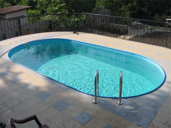 small inground swimming pools, blue oval shaped pool, filled with water, on a terrace with black metal fence