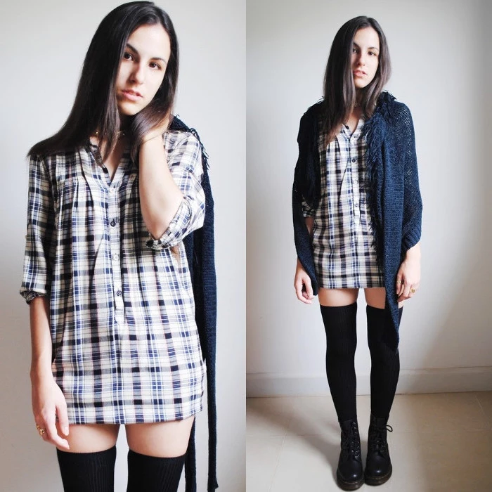 brunette young woman, wearing a white and blue checkered shirt, black over-the-knee socks, black combat boots, and a blue cardigan