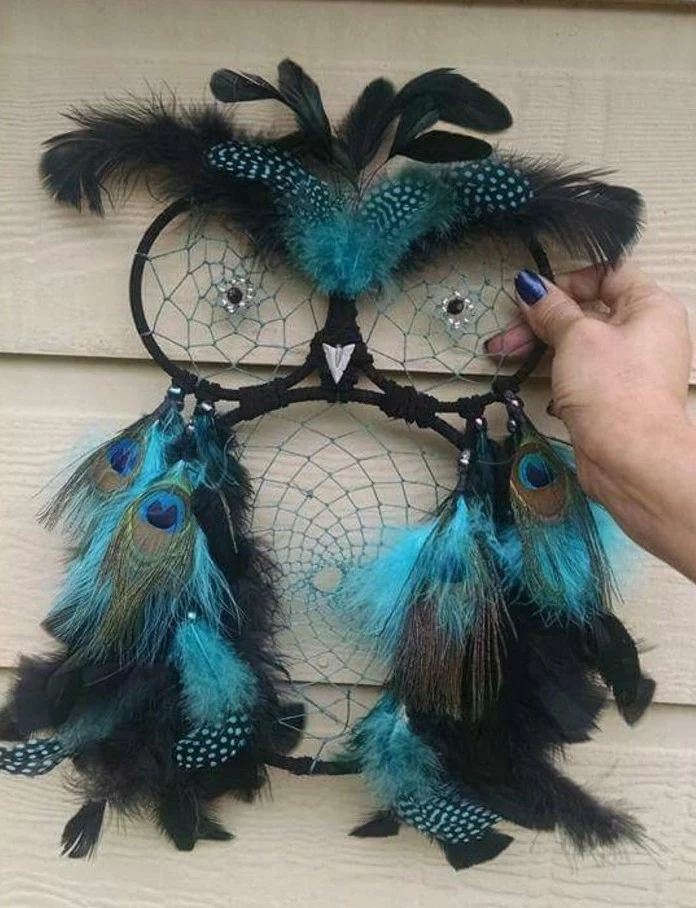 dreamcatcher designs, owl-shaped dream catcher in black, decorated with turquoise and black, spotted and peacock feathers, and held by a hand