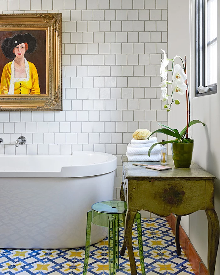diy bathroom décor, white subway wall tiles, and colorful blue, yellow and white floor tiles, in a room containing a white tub, a framed painting, and boho chic furniture 