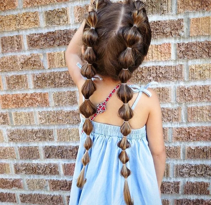 many rubber hairbands, decorating the two long pigtails, of a small child, in a pale blue summer dress